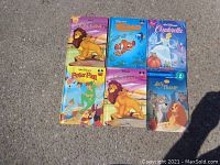 Six Disney children's storybooks arranged on the ground, including The Lion King in two editions, Finding Nemo, Cinderella, Peter Pan, and Lady and the Tramp.