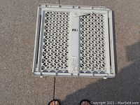 Folded view of the expandable gray plastic baby or pet gate showing lattice pattern and central locking mechanism.