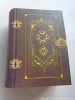 Front cover view of the book safe, showing brown faux leather texture with detailed gold ornamental embossing and three gold clasps.