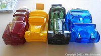 Four Avon collectible car-shaped bottles aligned side by side on a surface, showing colors and design details.