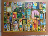 Completed jigsaw puzzle laid flat showing detailed whimsical artwork divided into rectangular sections with eclectic and colorful images.