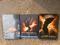 Three Batman movie cases placed side-by-side showing front covers - The Dark Knight, The Dark Knight Rises, Batman Begins