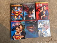 Six Superman-related DVDs on a carpeted floor including Lois & Clark seasons 1 and 2, Man of Steel, Superman Returns, Superman II