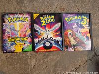 Three Pokémon DVD cases laid out on a carpeted floor: The First Movie, Pokémon 2000, and Pokémon The Movie 3