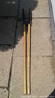 Full length view of the post hole digger showing wooden handles and metal digging blades.