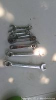 Top-down photo of seven assorted used wrenches on a light surface showing varying sizes and types.