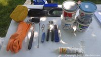 Photo showing a lot of tile working tools and adhesive containers arranged on a table outdoors.