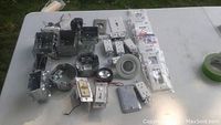 Various electrical components including multiple metal junction boxes, light fixture housing, wall plates, switches, and wiring parts laid out on white surface.