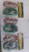 Photo showing three sets of red and green bungee cords, all sealed in plastic packaging with attached information cards.