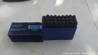 Box and 27 metal stamping letter stamps arranged inside blue plastic holder with box showing label information.