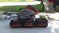 Photo of Milwaukee V28 6.5 inch circular saw and three red and black V28 Lithium-Ion batteries on a table outdoors.