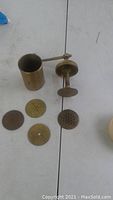 Small brass crank press disassembled showing main body, lever handle, and four brass perforated plates with various hole patterns.