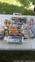 Multiple tubes of caulking glue and one manual caulking tool arranged on a white surface outdoors.