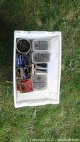 Large plastic tote with mixed nails, boxes, and containers inside, placed on grass.