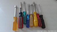 Front view of eight small nut drivers with assorted colored handles laid flat.