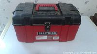 Closed red and black Craftsman tool box with a metal latch and red handle on top.