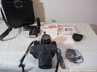 Full view of Pentax ME camera with leather half-case, battery grip/attachment, wiring cable, lens cap, instruction manual, and black Minolta Camera Co. Ltd shoulder bag.
