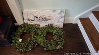 Abstract canvas wall art and two greenery wreaths on floor near stairs