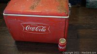 Red metal Coca Cola cooler with rust and dirt on top surface, soda can placed for size reference