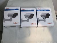 Front view of the three dummy security cameras in original white boxes with blue accents, showing product image and brand name 'Recess'.