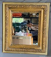 Front view of the antique mirror showing ornate gold tone intricately carved frame and clear mirror surface reflecting a room.