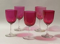 Front angle view showing five cranberry glass sherry glasses with varying sizes and clear stems, highlighting the color and shape of each glass.