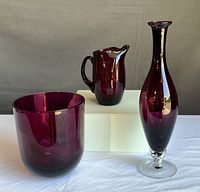 All three aubergine colored art glass pieces: tall vase, pitcher, and wide vase on white background