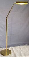 Full view of the brass floor task lamp in standing position with lamp turned on.