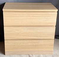 Front view of a contemporary three-drawer dresser made of light wood, showing clean flat drawer fronts without handles.