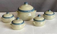 Photo showing set of one large covered soup tureen and four smaller covered soup bowls, cream color with blue accents.