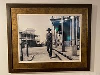 Framed black and white Western print with a man walking on a wooden sidewalk and period buildings in the background.