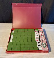 Opened red case containing Mahjong tiles arranged neatly with some tiles revealed showing Chinese characters.