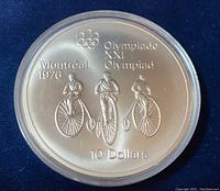 Obverse side of the coin showing cycling theme with three vintage bicycle riders and Olympic references.