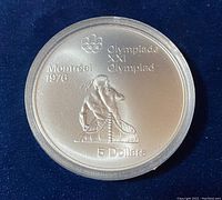 Obverse side showing Montreal 1976 Olympic emblem, canoeing theme design, and 5 dollar denomination in sealed case.