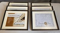 Overview photo showing six identical black document frames with matting and glass laid out in two rows of three frames each on a beige surface.