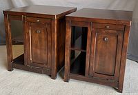 Front view of the pair of wooden end tables showing drawer, cabinet door, and open side shelving.