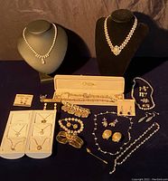 Wide shot of the assorted jewelry laid out including necklaces on busts, earrings on cards, brooches, and pins on table