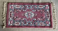 Top view of the small rectangular pink carpet with a floral and ornamental pattern, showing one side of the fringe.