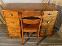 Front view of the solid wood desk with matching chair showing seven drawers and brass knobs, decorative detailing below center drawer, and small crack at corner.