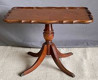 Front view of vintage wooden occasional table with flip top down, showing scalloped edge and central pedestal base with brass feet caps.