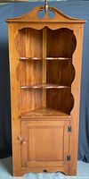 Full front view of the wooden corner cabinet showing shelves and door.