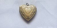 Front view of vintage heart-shaped metal locket showing detailed floral and heart engravings.