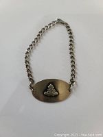 Front side showing an oval sterling silver plate with a raised combat engineer badge and chain bracelet.