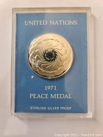 Front view of the United Nations Peace Medal sealed in clear plastic case with blue background card showing 'UNITED NATIONS', date 1971, 'PEACE MEDAL', and 'STERLING SILVER PROOF'.