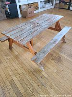 Solid wood picnic table with visible weathering and wear, photographed from a side angle showing one attached bench and the wooden floor underneath.
