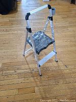 Drywalling stool front view showing metal frame with paint splatters and black cushioned seat with wear.