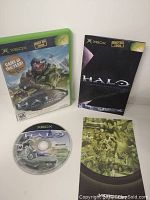 Photo showing original Xbox game case, metal collector's case, game disc, and manual for Halo Combat Evolved