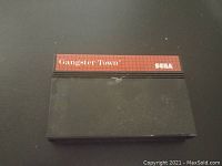 Front view of the black Sega Master System cartridge for the game Gangster Town, showing red and black label with text.