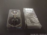 Front view of Batman logo keychain inside clear plastic case with packaging branding and design visible.
