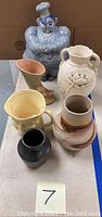 Photo of six pottery items on a table including Redwing clown cookie jar, multiple vases, and a pitcher for lot photography.